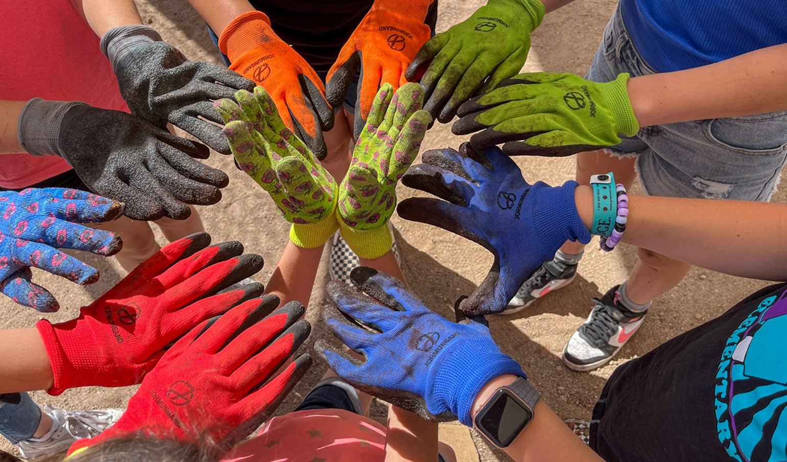 Students wearing colorful gardening gloves join hands in a circle, symbolizing teamwork and collaboration.